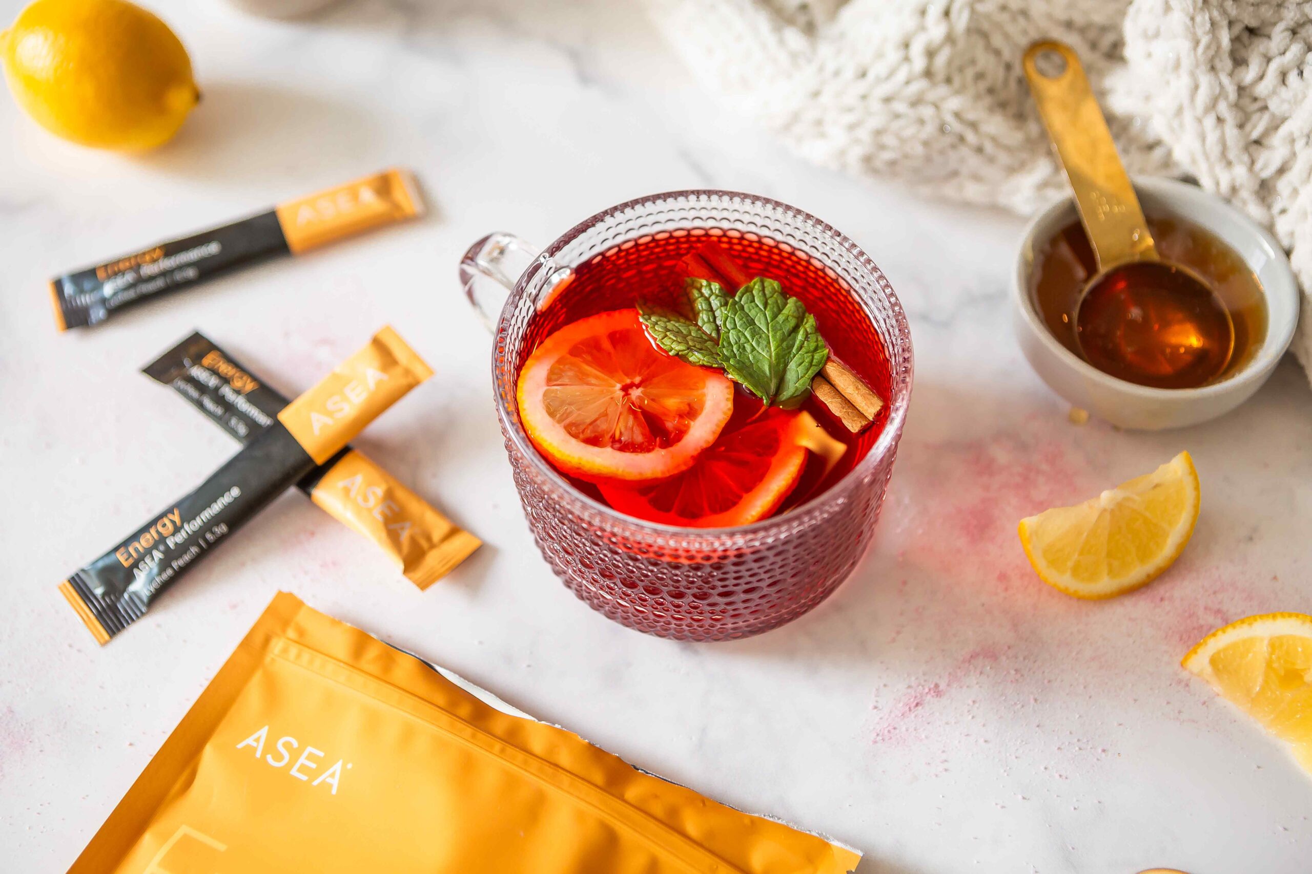A warm mug of hibiscus tea with fresh lemon slices, honey, and ASEA Energy stick packs arranged on a light surface, showcasing a clean and refreshing morning energy ritual.