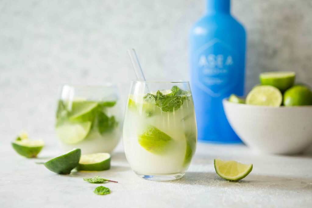 A fresh citrus drink with lime and mint is displayed alongside the blue ASEA Redox bottle, visually representing hydration support and cellular-level wellness.