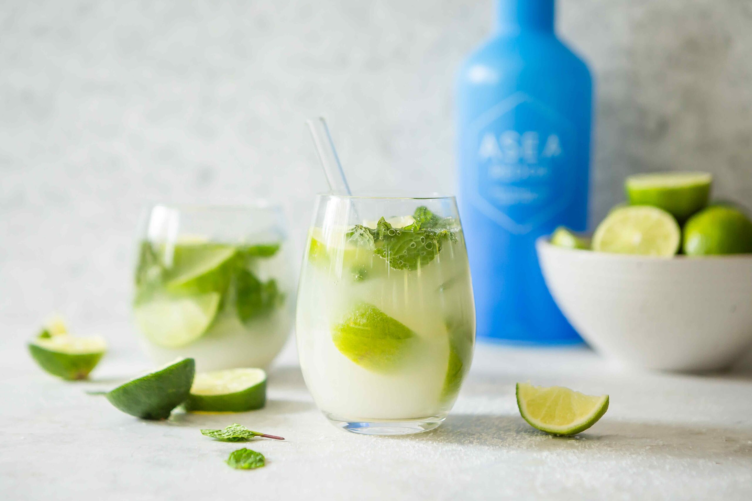 A fresh citrus drink with lime and mint is displayed alongside the blue ASEA Redox bottle, visually representing hydration support and cellular-level wellness.