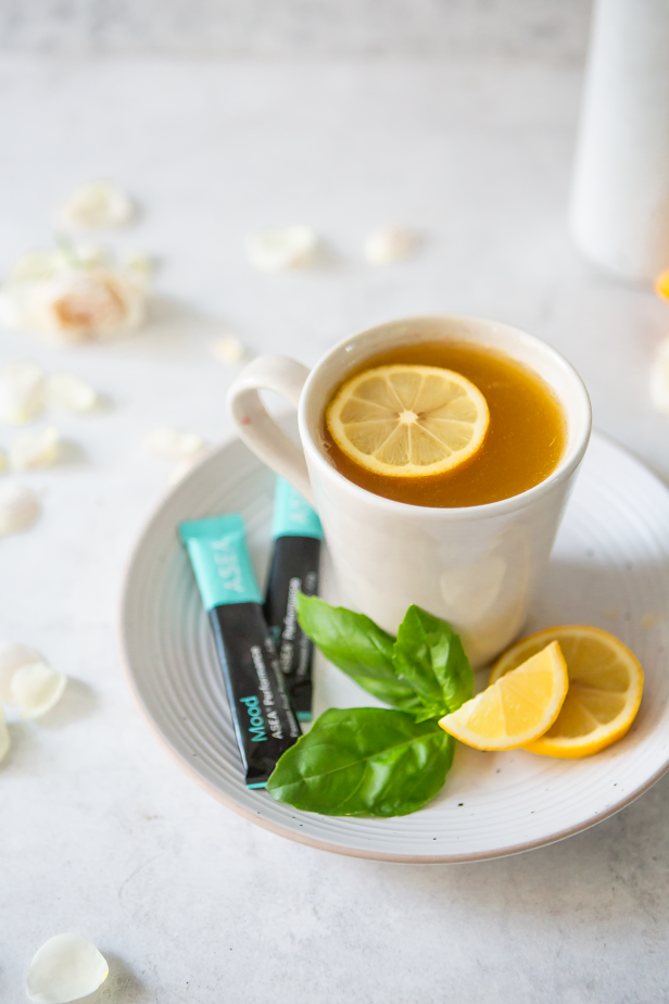 An overhead view of mood boosting tea ingredients, including chamomile tea, fresh lemon, basil, and ASEA Mood stick packs, highlights the mindful preparation behind this calming drink.