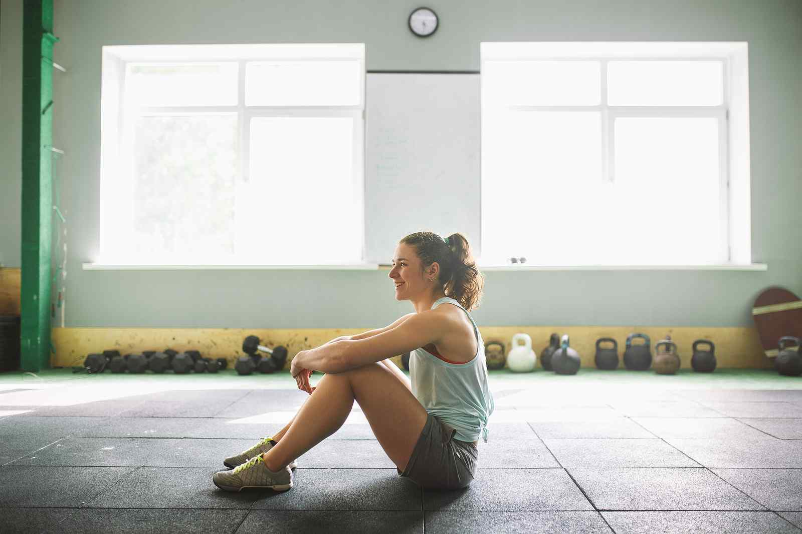 A woman sits calmly on a gym floor in a bright, open space, reflecting a balanced lifestyle that supports gut health, immune function, and overall microbiome support.