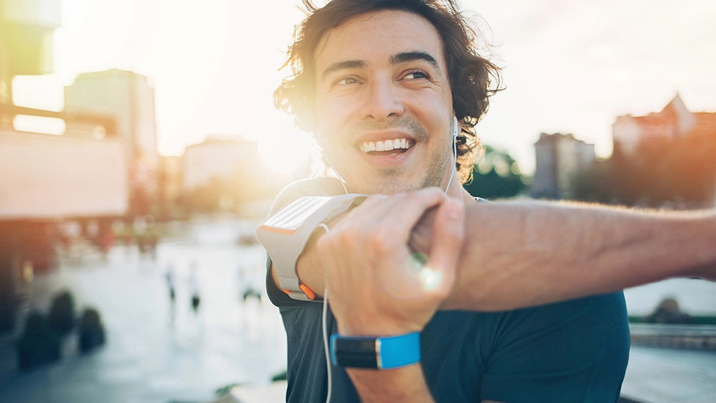 Mann dehnt sich im Freien und nutzt ein Fitnessarmband zur Beobachtung seiner körperlichen Aktivität